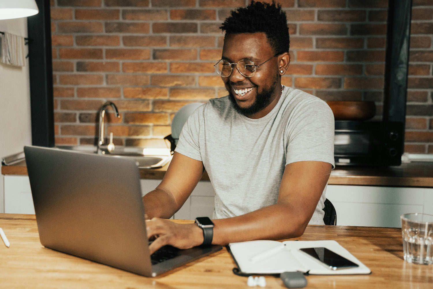 Man using a laptop at a kitchen counter with a brick wall background